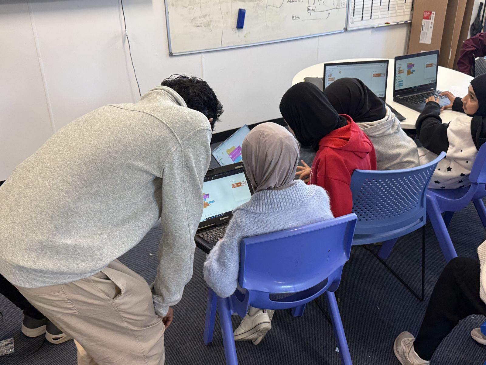 A mentor helping a student with code on a laptop
